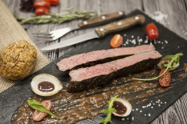 Sebze ve barbekü soslu mermer dana eti nden Ribeye biftek. Çatal ve bıçak ile siyah taş bir tabak üzerinde servis . — Stok fotoğraf