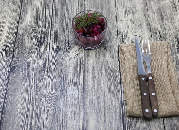 Ensalada de remolacha en jarrón de vidrio con tenedor y cuchillo sobre fondo de madera . — Foto de Stock