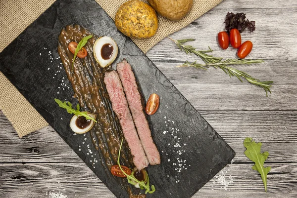 Sebze ve barbekü soslu mermer dana eti nden Ribeye biftek. Çatal ve bıçak ile siyah taş bir tabak üzerinde servis .