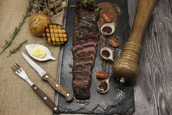 Delicious juicy hot roast beef cut into delicious pieces of meat and vegetables. Served on a black stone plate with a fork and knife and pepper. — Stock Photo, Image