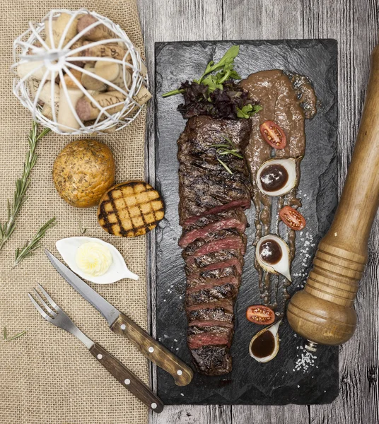 Lezzetli sulu sıcak biftek et ve sebze lezzetli parçalara. Bir siyah taş bir çatal ve bıçak ve biber ile tabakta. — Stok fotoğraf