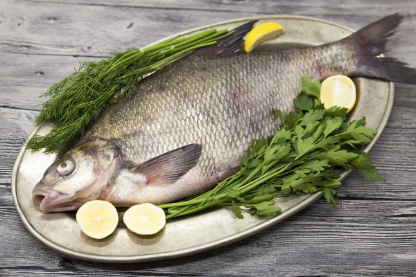 Un grosso pesce vivo orata fiume pesce sdraiato su un su un vassoio di ferro con un coltello e fette di limone e con aneto sale — Foto Stock