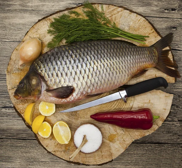 Φρέσκο ωμό ψάρι κυπρίνος αλιεύονται ψέματα σε ένα ξύλινο κούτσουρο με ένα μαχαίρι και φέτες λεμονιού και με αλάτι άνηθο. Ζωντανά ψάρια crucian Carassius auratus gibelio. — Φωτογραφία Αρχείου