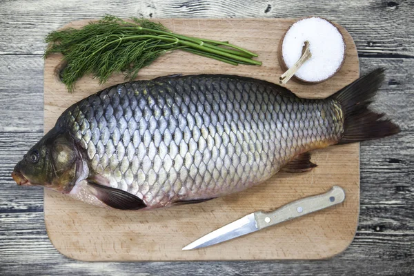 A large fresh carp live fish lying on a wooden board with salt and dill. — Stockfoto