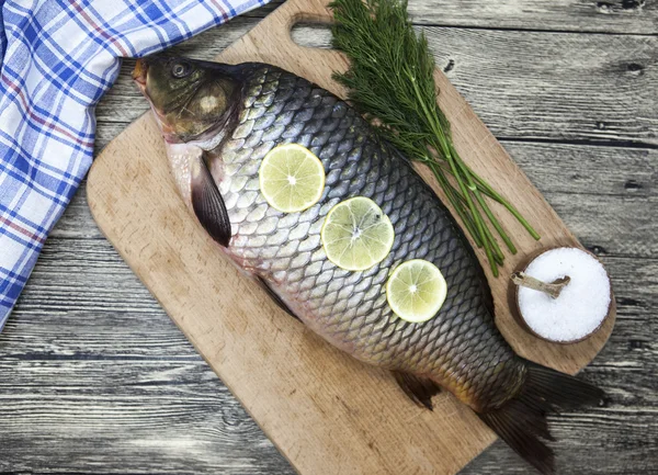 Una grande carpa fresca di pesce vivo sdraiato su un con un coltello e fette di limone e con aneto sale . — Foto Stock