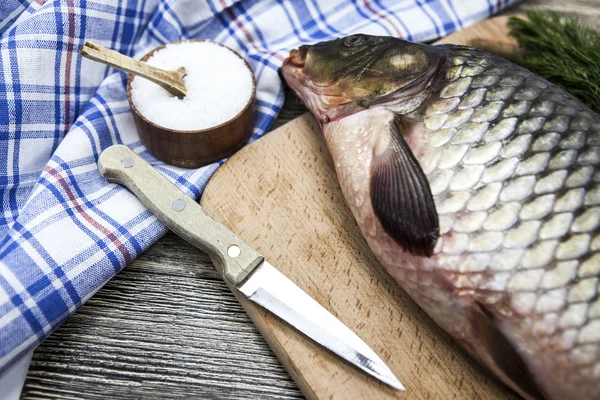 A large fresh carp live fish lying on a wooden board with a knife and slices of lemon and with salt dill.