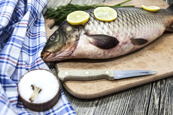 Una grande carpa fresca di pesce vivo sdraiata su una tavola di legno con un coltello e fette di limone e con aneto salato . — Foto Stock