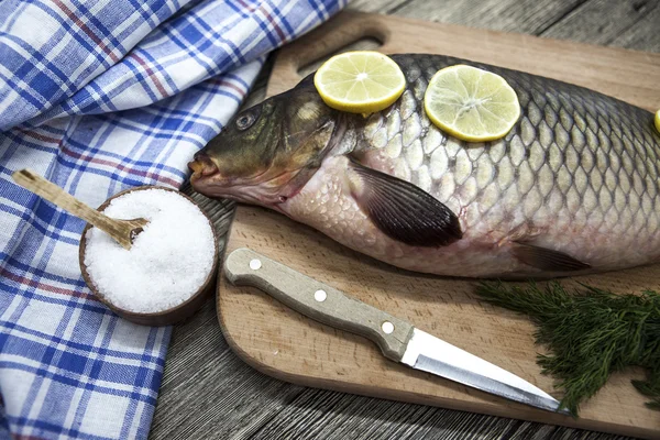 Una grande carpa fresca di pesce vivo sdraiata su una tavola di legno con un coltello e fette di limone e con aneto salato . — Foto Stock