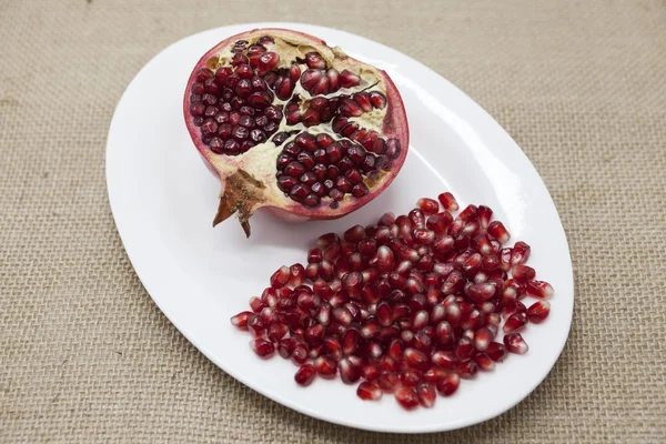 Pomegranates have broken into pieces with red berries on a porcelain plate on a textile background. — Stock Photo, Image