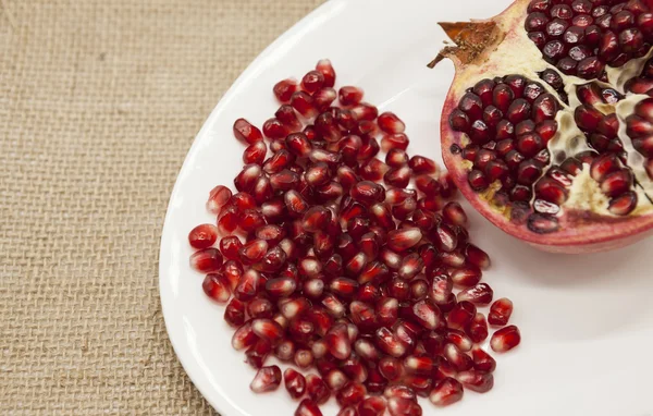 석류는 섬유 배경에 도자기 접시에 붉은 열매와 함께 조각으로 깨진 있다. — 스톡 사진