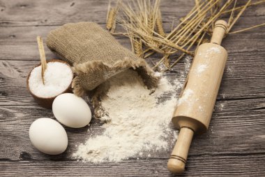 Wheat flour in a canvas bag, with spikelets of rye, a large salt shaker wood, raw eggs, a wooden rolling pin: set for making homemade bread dough on a beautiful dark wooden background