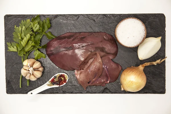 Trozos de hígado fresco de res cruda, cebolla, ajo, especias, sal en el plato de piedra sobre un fondo blanco . — Foto de Stock