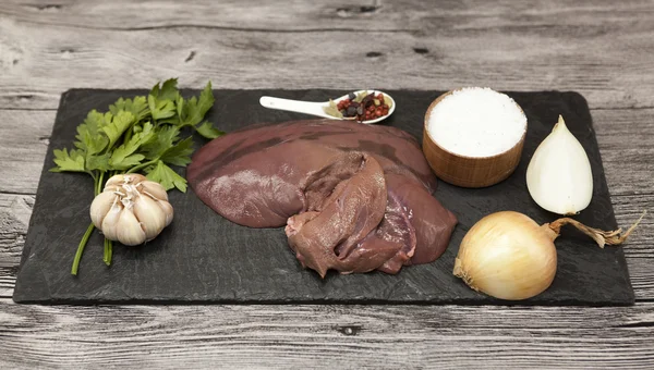 Trozos de hígado fresco de res cruda, cebolla, ajo, especias, sal en el plato de piedra sobre un fondo blanco . — Foto de Stock