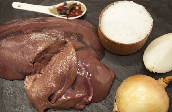 Primer plano de trozos de hígado fresco de res cruda, cebolla, ajo, especias, sal en el plato de piedra sobre un fondo blanco — Foto de Stock