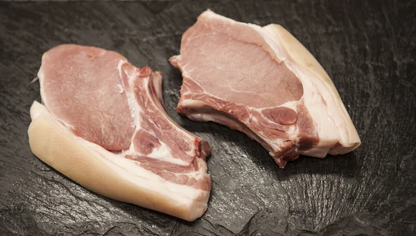 Trozos de cerdo fresco crudo apetitoso primer plano sobre fondo de piedra negra —  Fotos de Stock