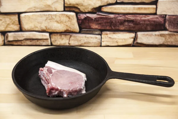 A piece of delicious fresh raw pork close-up on a cast iron skillet on the table rustic kitchen. — Zdjęcie stockowe