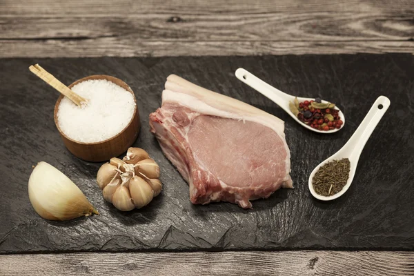 Trozos de cebolla de cerdo fresca cruda, ajo, especias, sal en el plato de piedra —  Fotos de Stock