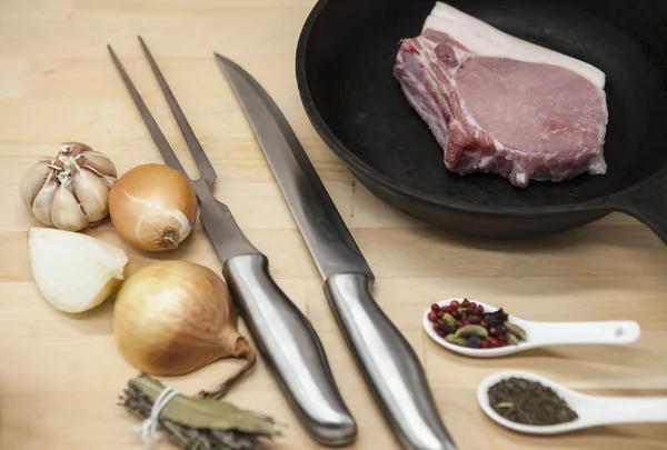 Kawałek szczegół widelec zachwycający świeży wieprzowa, nóż, przyprawy, cebula, czosnek, na patelni żeliwnych na stole rustic kitchen. — Zdjęcie stockowe