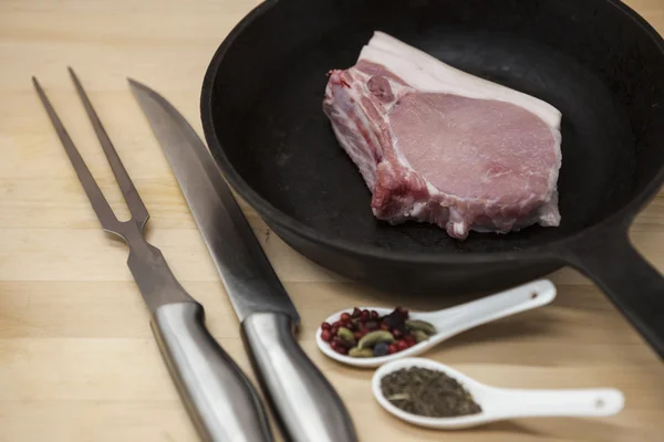 Kawałek szczegół widelec zachwycający świeży wieprzowa, nóż, przyprawy, cebula, czosnek, na patelni żeliwnych na stole rustic kitchen. — Zdjęcie stockowe