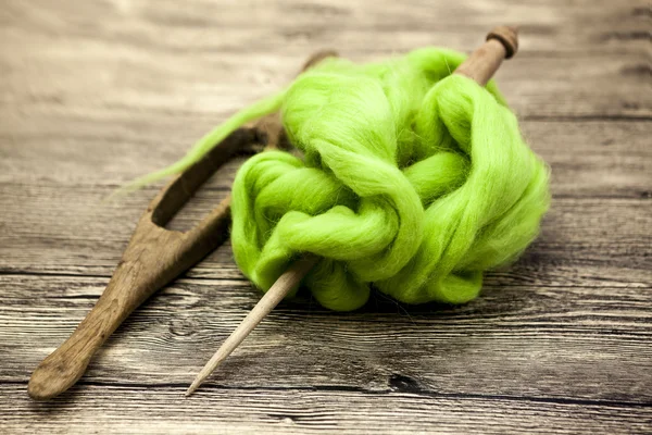 Green wool and old spindle close-up on wooden background. Tools for knitting of wool — Stock Photo, Image