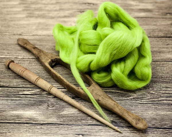 Green wool and old spindle close-up on wooden background. Tools for knitting of wool — Stock Photo, Image