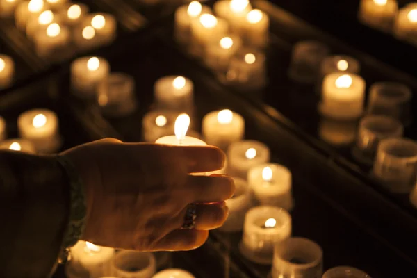 Burning candles in a church with the hand of an old woman close-up. Royalty Free Stock Images