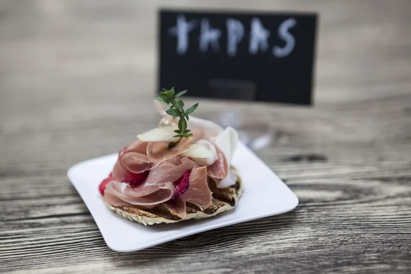 Fresh delicious Spanish tapas with hamon with fresh herbs and strawberries with poster TAPAS on the  wooden background . Great background for restaurant, cafe — Stock Fotó