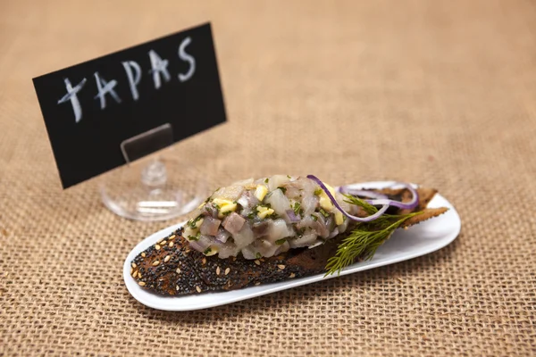 TAPAS poster . Fresh, delicious Spanish tapas with Tartar of herring and onions on a black baguette. An excellent background for the menus, cafe, restaurant. — Stock Fotó