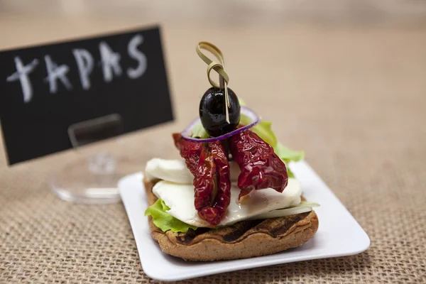 Deliciosas tapas espanholas, com uma mussarela rústica e tomate seco com azeitona. Cartaz TAPAS  . — Fotografia de Stock