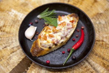 Home baked hot sandwich with tomato, salami, cheese, onion, chile pepper, garlic  on a cast-iron pan on a wooden background.