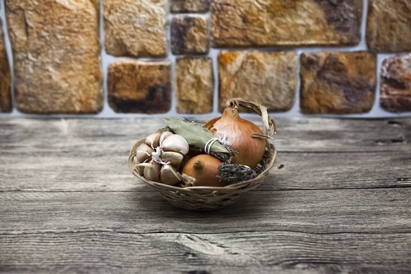 Gewürzset im Weidenkorb Zwiebeln, Provence-Kräuter, Knoblauch am Tisch in der Küche — Stockfoto