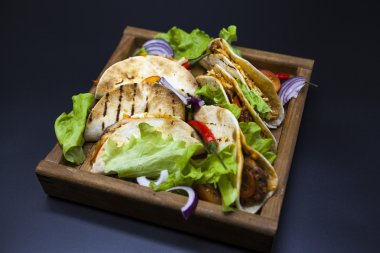 Mexican Tortilla with meat, beef and stewed vegetables and spicy sauce on a wooden tray.