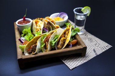 Mexican Tortilla with meat, beef and stewed vegetables and spicy sauce with a shot of tequila and lime on a wooden tray.