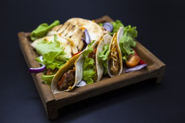 Mexican Tortilla with meat, beef and stewed vegetables and spicy sauce on a wooden tray.