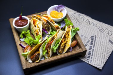Mexican Tortilla with meat, beef and stewed vegetables and spicy sauce on a wooden tray.