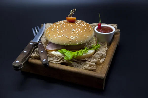 Klassische amerikanische frische saftige Burger mit Huhn und Schinken auf einem hölzernen Tablett mit einer würzigen Chilisoße. schönes Foto auf dunklem Hintergrund — Stockfoto