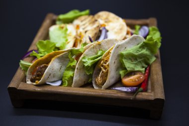 Mexican Tortilla with meat, beef and stewed vegetables and spicy sauce on a wooden tray.