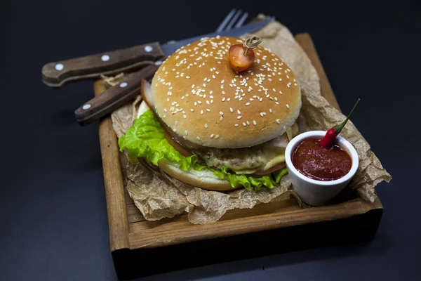 Klassische amerikanische frische saftige Burger mit Huhn und Schinken auf einem hölzernen Tablett mit einer würzigen Chilisoße. schönes Foto auf dunklem Hintergrund — Stockfoto