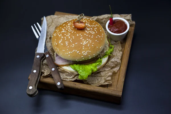 Klassische amerikanische frische saftige Burger mit Huhn und Schinken auf einem hölzernen Tablett mit einer würzigen Chilisoße. schönes Foto auf dunklem Hintergrund — Stockfoto