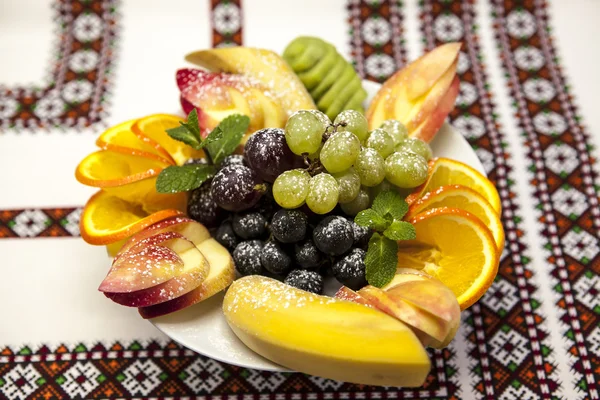 Placa con frutas frescas para las fiestas: plátano, uvas, naranja, manzana, kiwi, menta —  Fotos de Stock