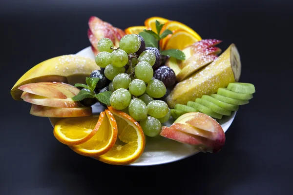 Prato com frutas frescas para as férias: banana, uvas, laranja, maçã, quivi, hortelã — Fotografia de Stock