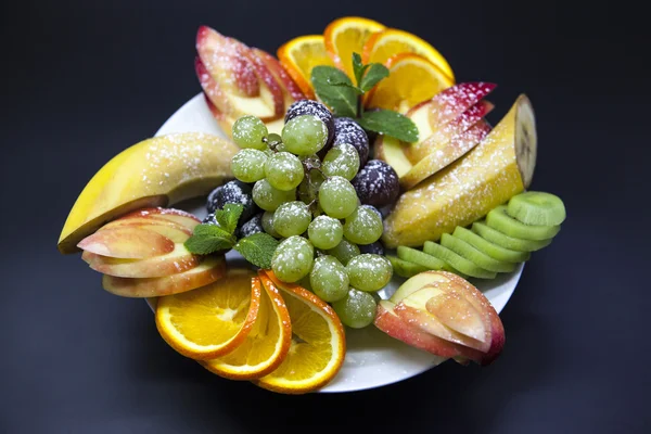 Teller mit frischem Obst für die Feiertage: Banane, Trauben, Orange, Apfel, Kiwi, Minze — Stockfoto