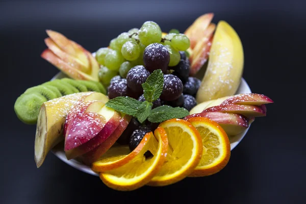 Plate with fresh fruits for the holidays: banana, grapes, orange, apple, kiwi, mint — Stock Photo, Image