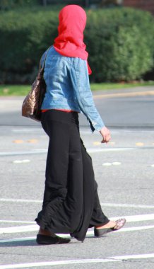 Kafasında kırmızı bir eşarpla caddeden karşıya geçen Müslüman bir kadın..