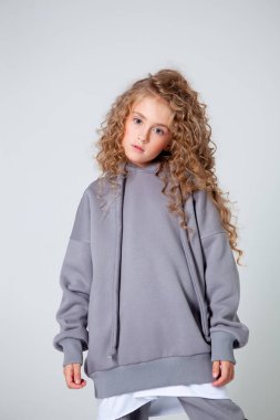 Uzun kollu beyaz tişörtlü kıvırcık kız duruyor.