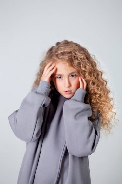 Uzun kollu beyaz tişörtlü kıvırcık kız duruyor.