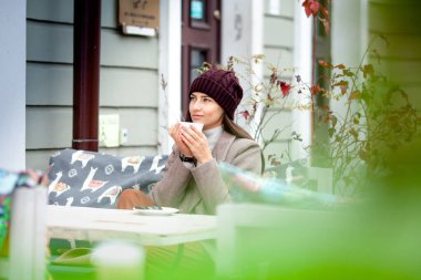 Uzun saçlı esmer, bir sokak kafesinin masasında kahve içiyor.