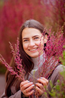 Bitkilerin arka planında açık bej ceketli uzun saçlı esmer.