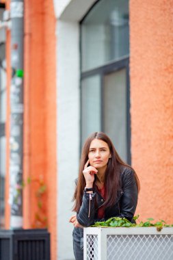 Eski bir binanın arka planında deri ceketli, uzun saçlı esmer.