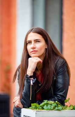 Eski bir binanın arka planında deri ceketli, uzun saçlı esmer.